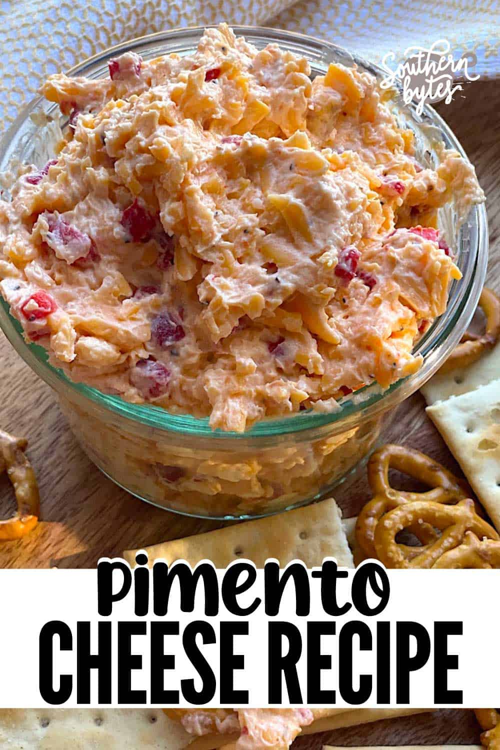 A pin image of a glass bowl of homemade pimento cheese surrounded by pretzels and crackers.