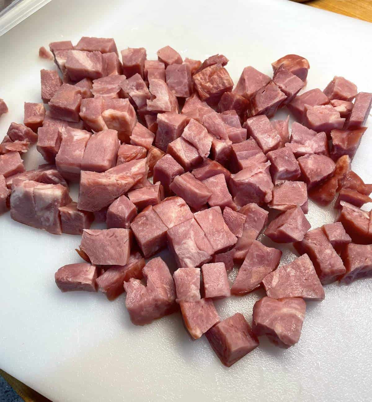 Diced seasoning ham on a white cutting board.