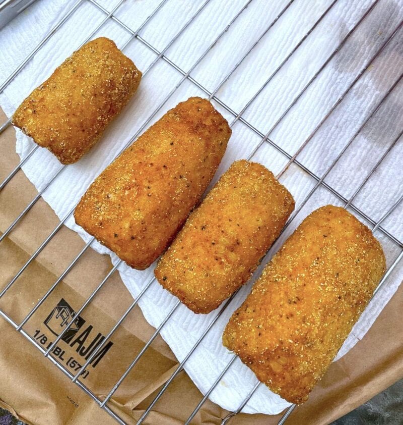 Four pieces of fried corn on the cob draining on a rack over paper towels.