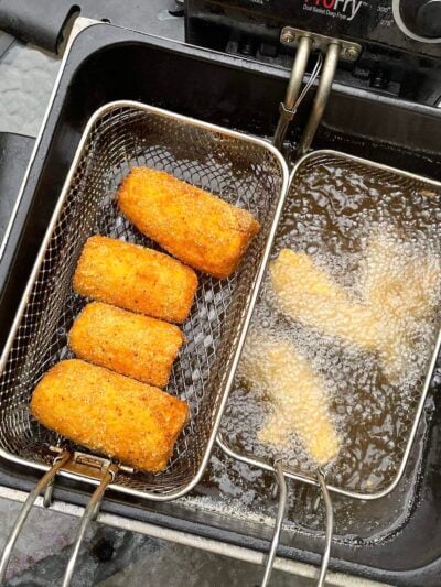 Four pieces of fried corn draining in a basket in a deep fryer.