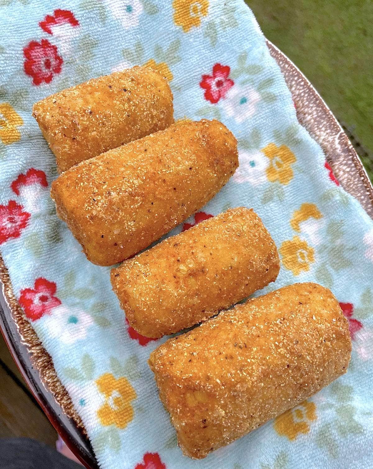 Four pieces of fried corn on the cob on a blue towel on a plate.