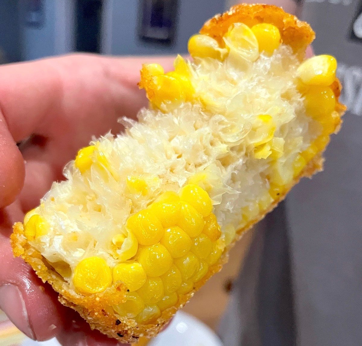 A hand holding a piece of fried corn on the cob with a few bites taken out of it.