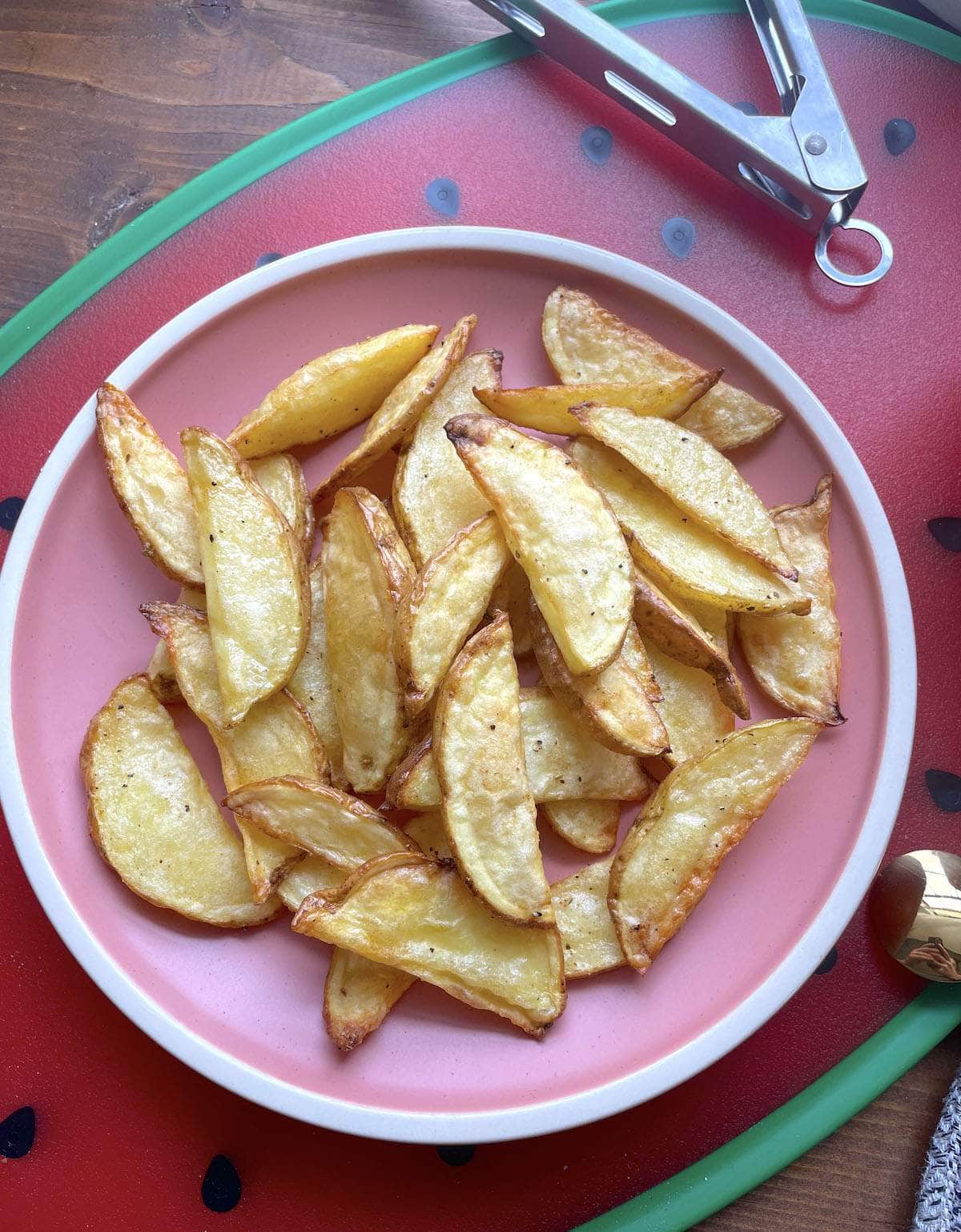 A pink plate with air fried potato wedges on it.