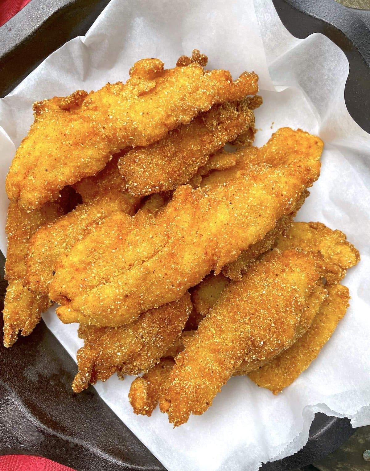 A pile of cornmeal breaded fried fish sitting in a cast iron pan.