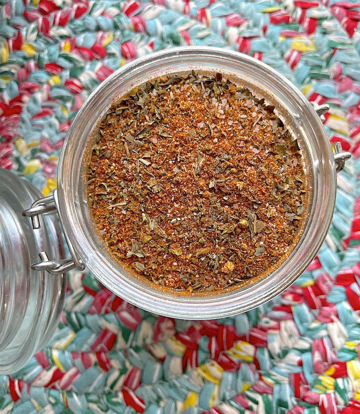 A jar of homemade creole seasoning blend on a colorful mat.