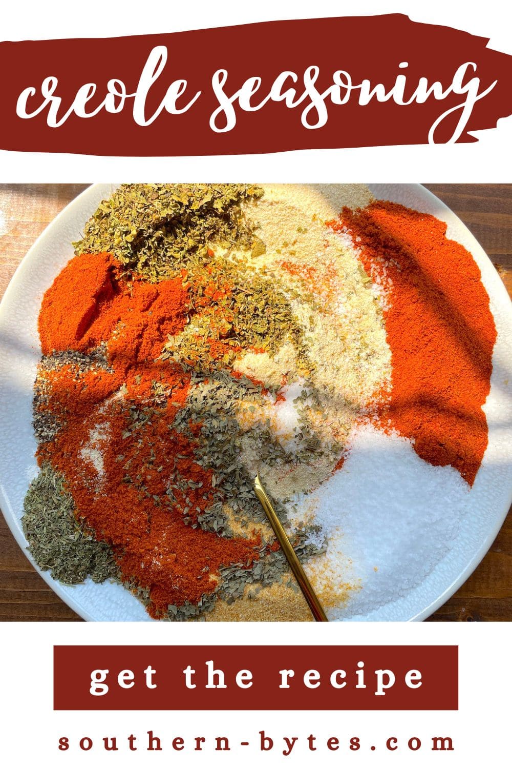 A pin image with a white plate with the ingredients in creole seasoning mixed up on it with a gold spoon.