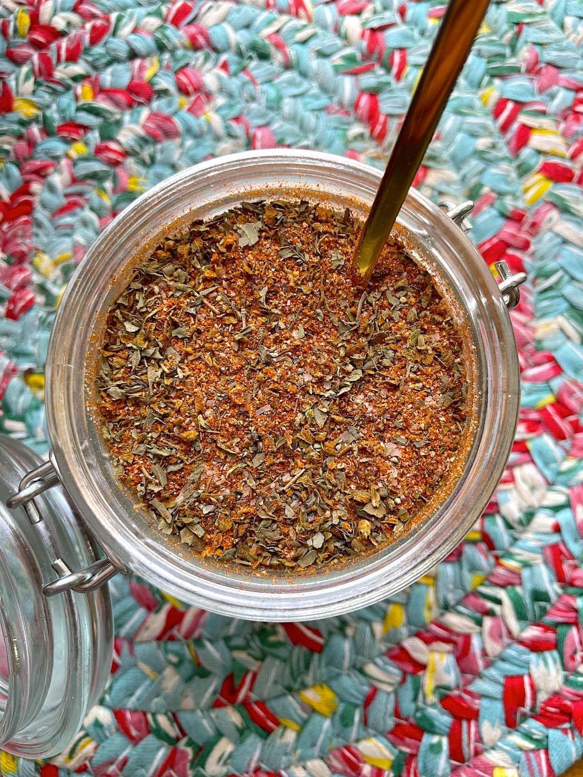 A jar of homemade creole seasoning on a colorful mat with a gold spoon in the jar.