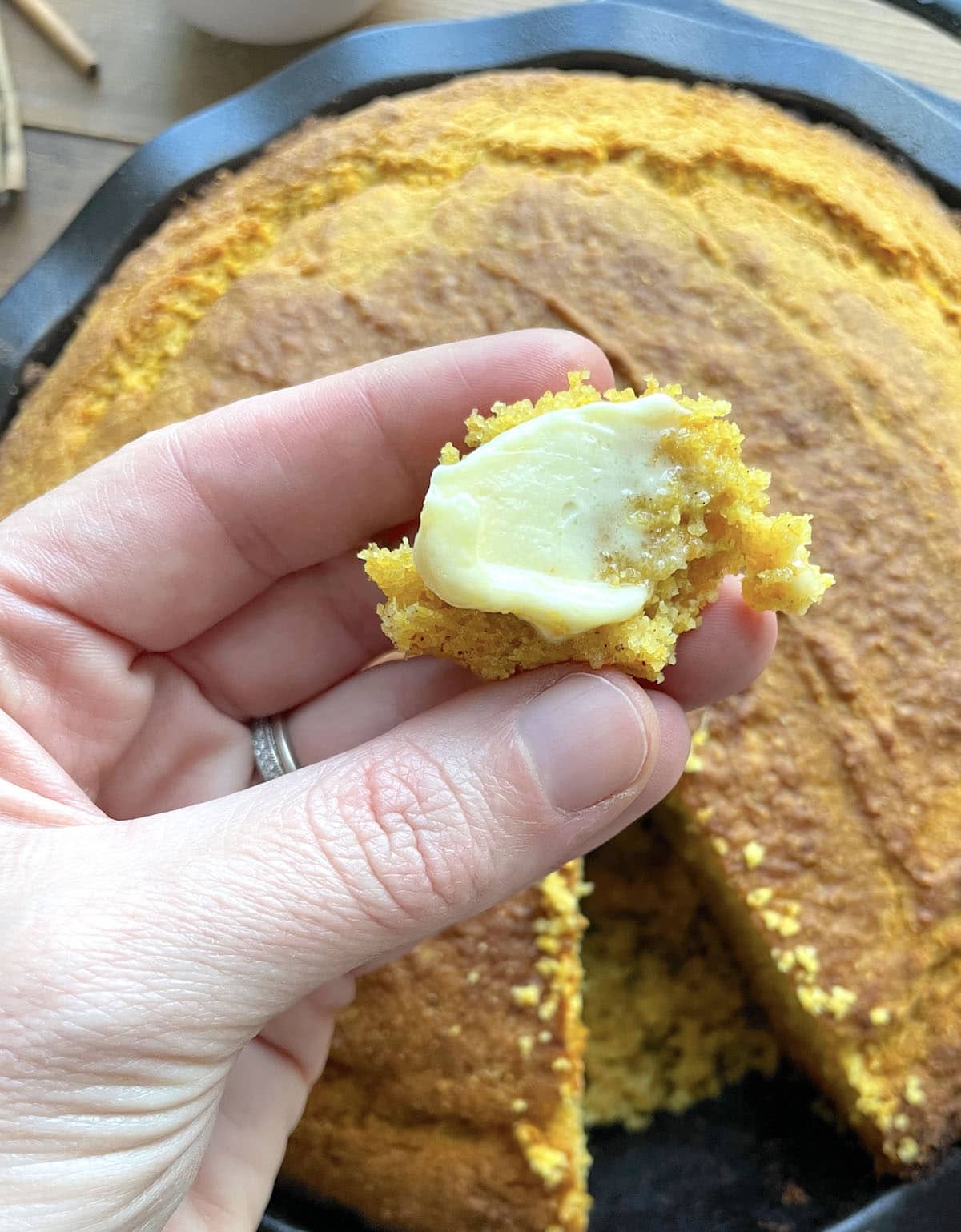 A hand holding sweet potato cornbread with a smear of honey butter on it.