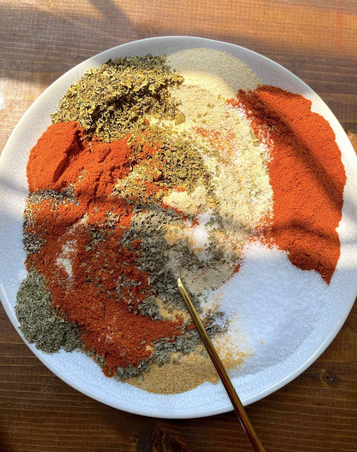 A white plate with the ingredients in creole seasoning mixed up on it with a gold spoon.