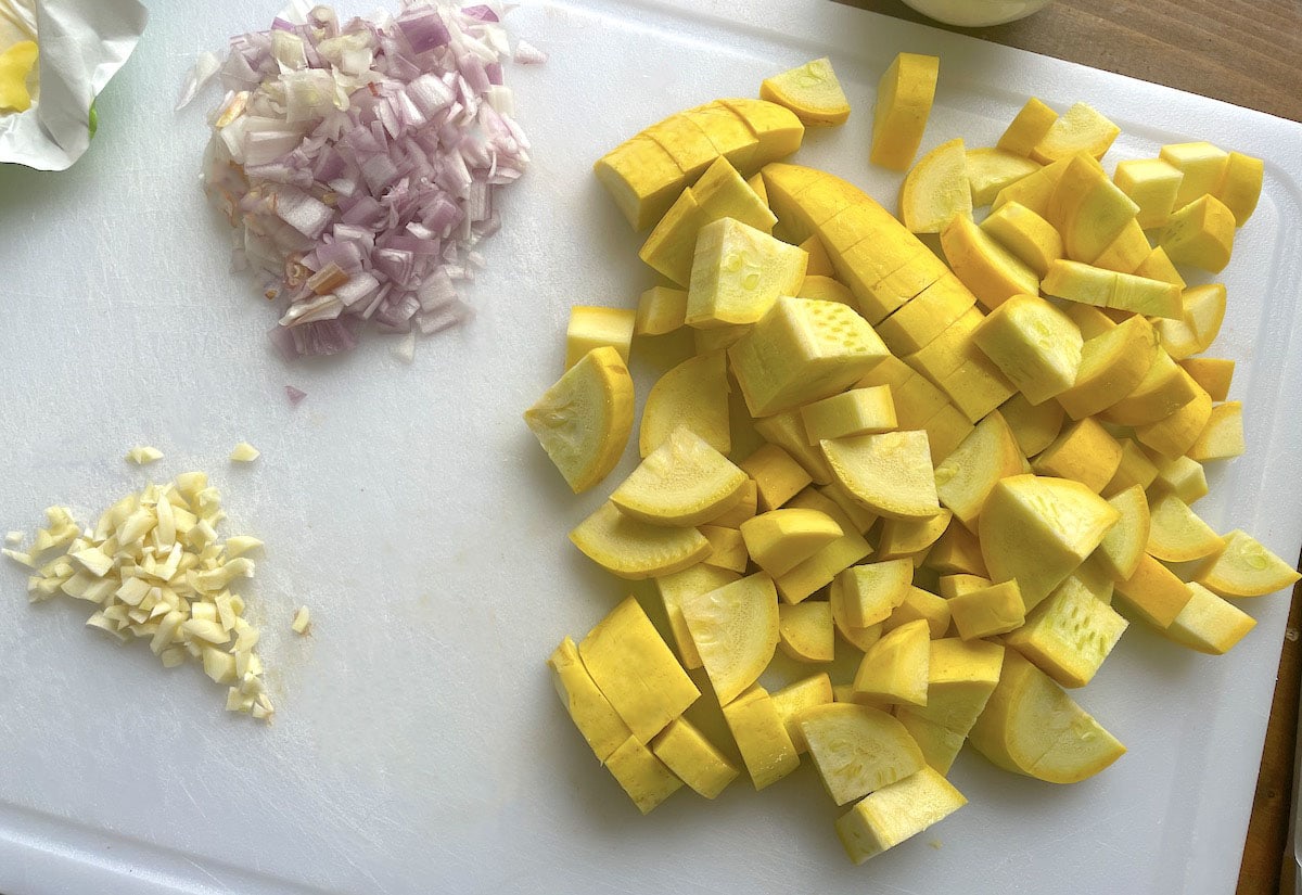 Diced yellow squash, garlic, and shallots on a white cutting board.