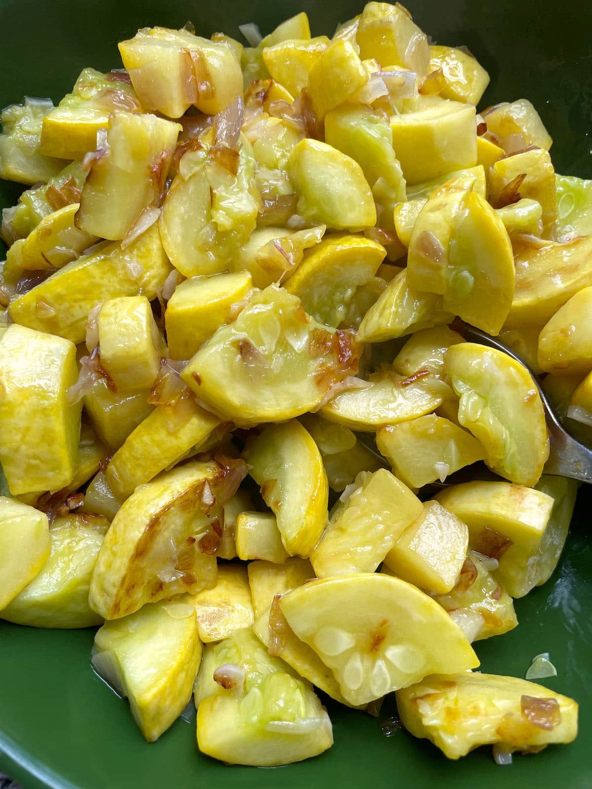 A green bowl filled with sauteed yellow squash and onions.