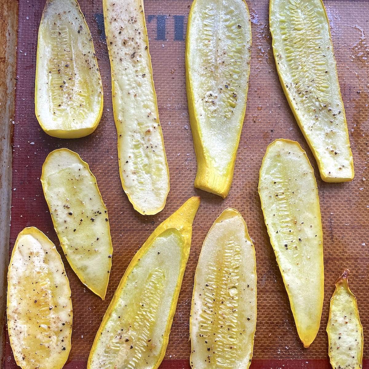 Oven roasted yellow squash strips on a lined baking sheet.