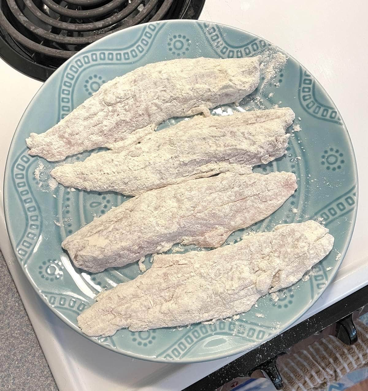 Trout fillets coated in flour on a blue plates.