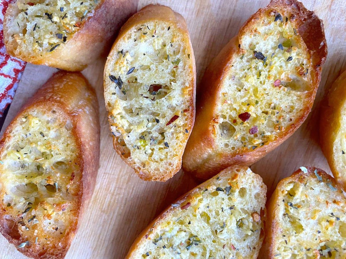 Slices of garlic toast topped with Italian seasoning on a wooden board.