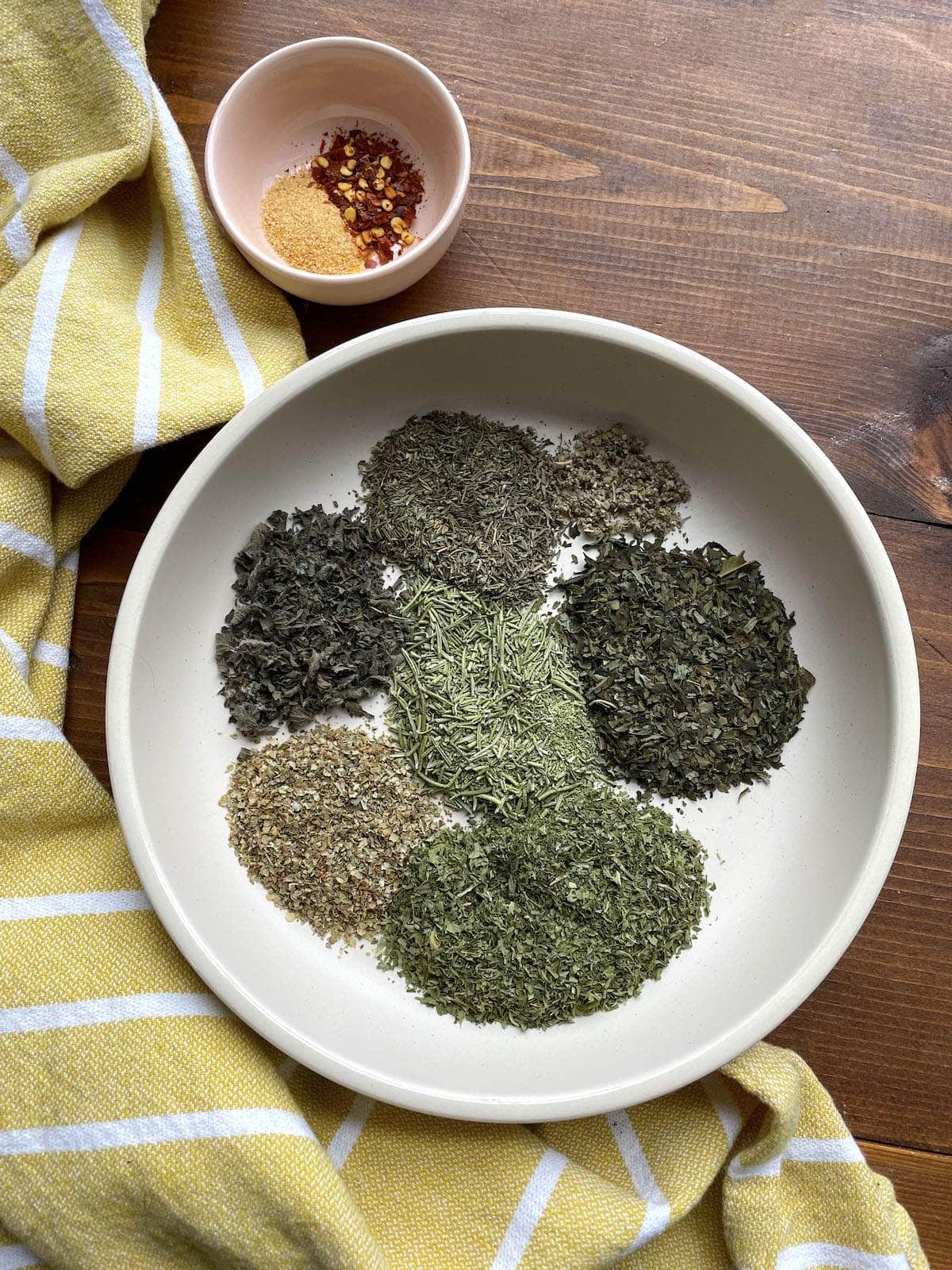 The ingredients in Italian seasoning in a large gray bowl, spread out in piles.