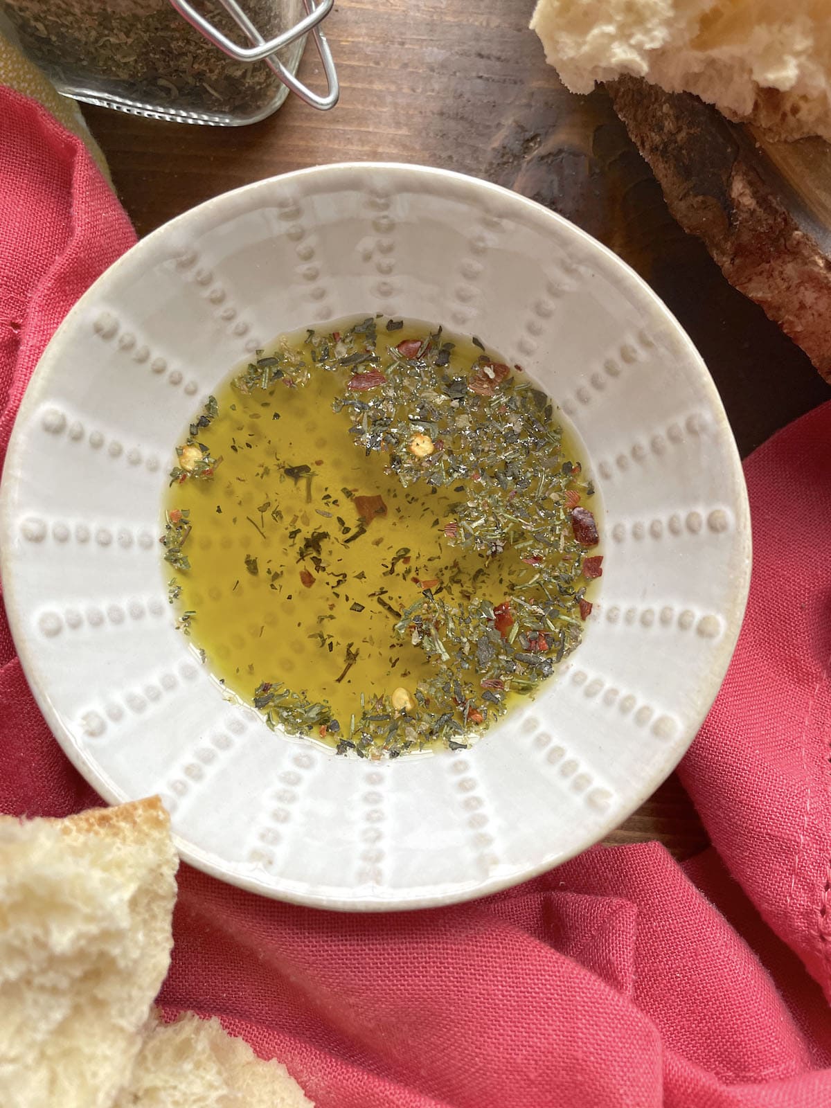 A small bowl of olive oil with Italian seasoning in it and torn pieces of bread around it.