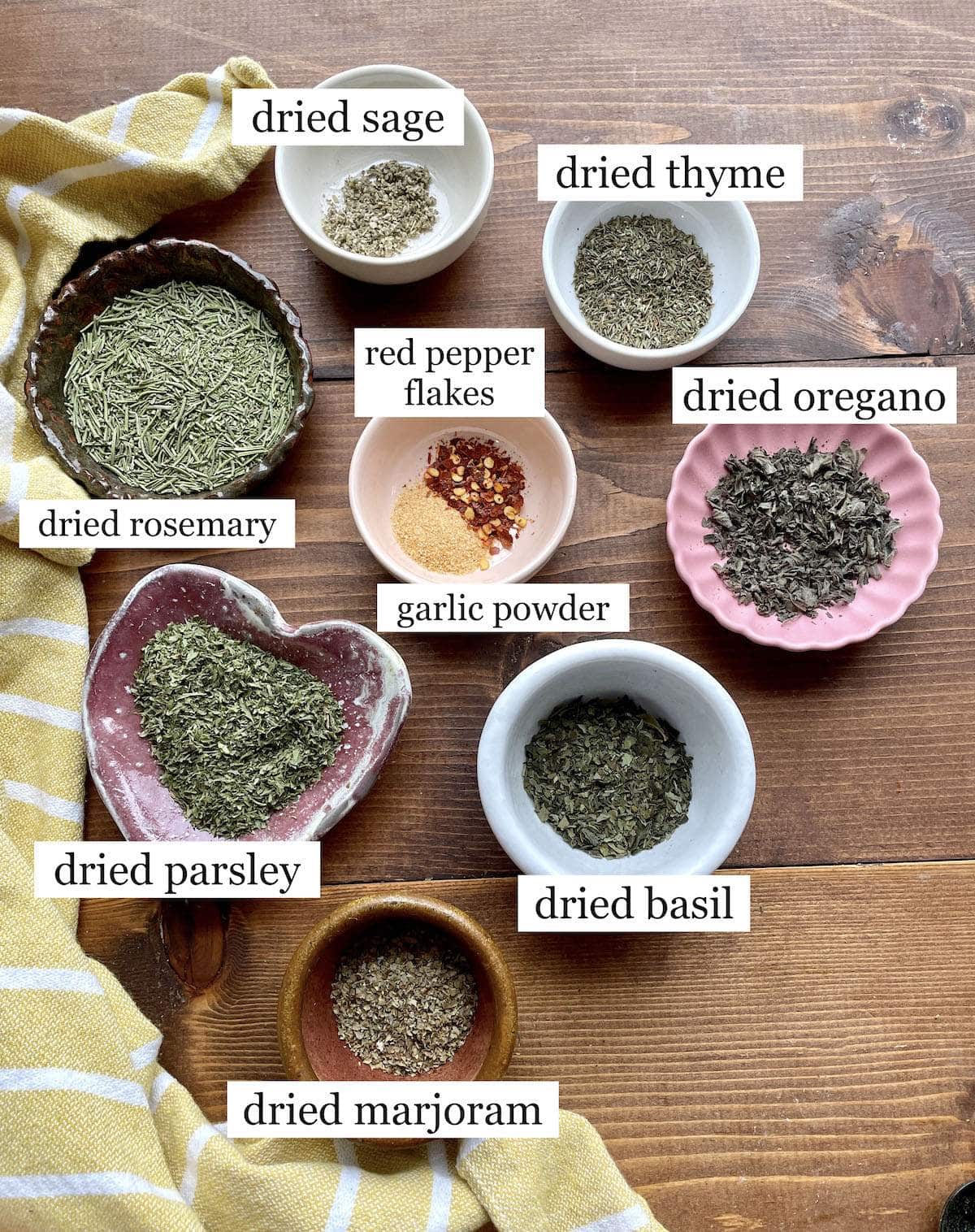 The ingredients in Italian seasoning in small bowls, laid out and labeled.