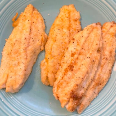 A blue plate with pan fried fish fillets on it.