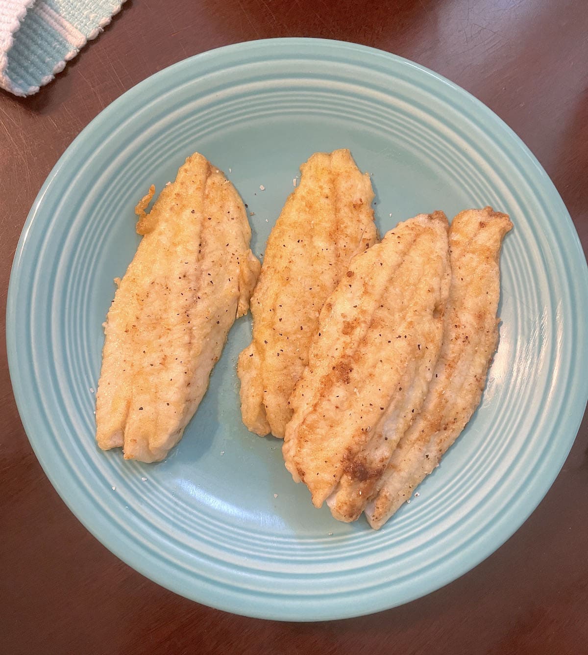 Four pan fried trout fillets on a blue plate.