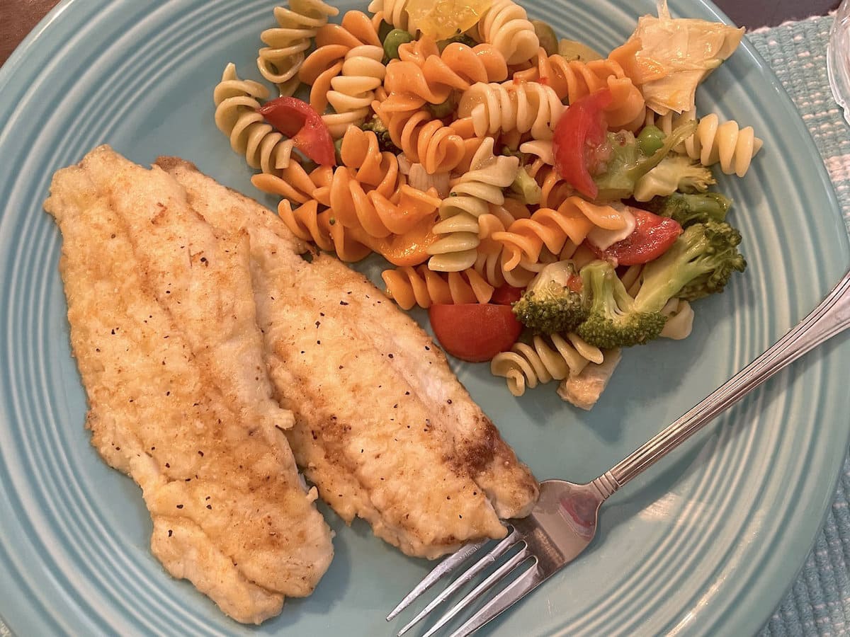 A blue plate with pan fried fish fillets and pasta salad on it.