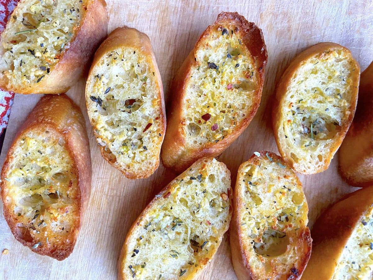 Slices of garlic toast with Italian seasoning on a wood cutting board.