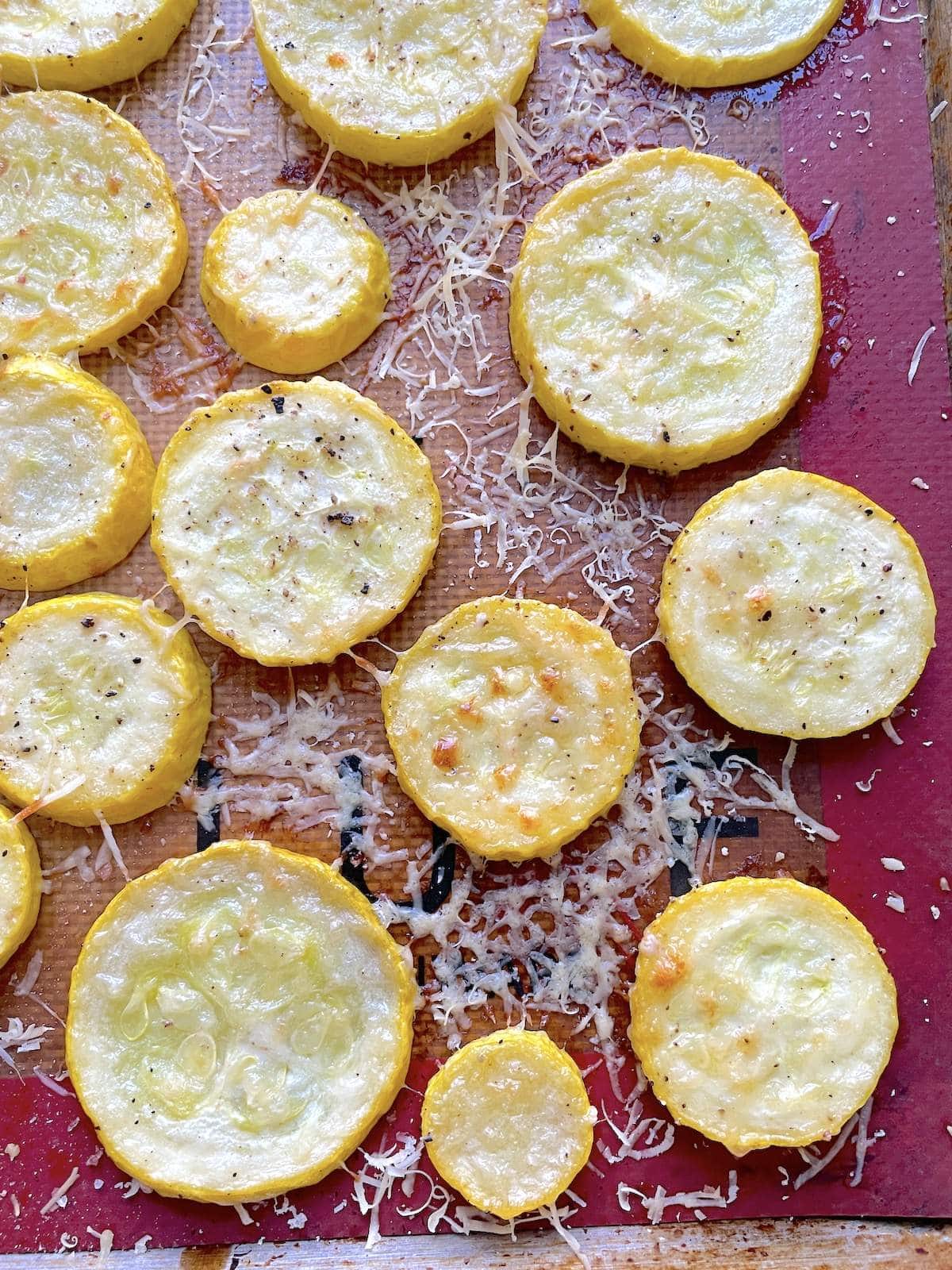 Roasted sliced squash rounds on a baking sheet topped with parmesan cheese.