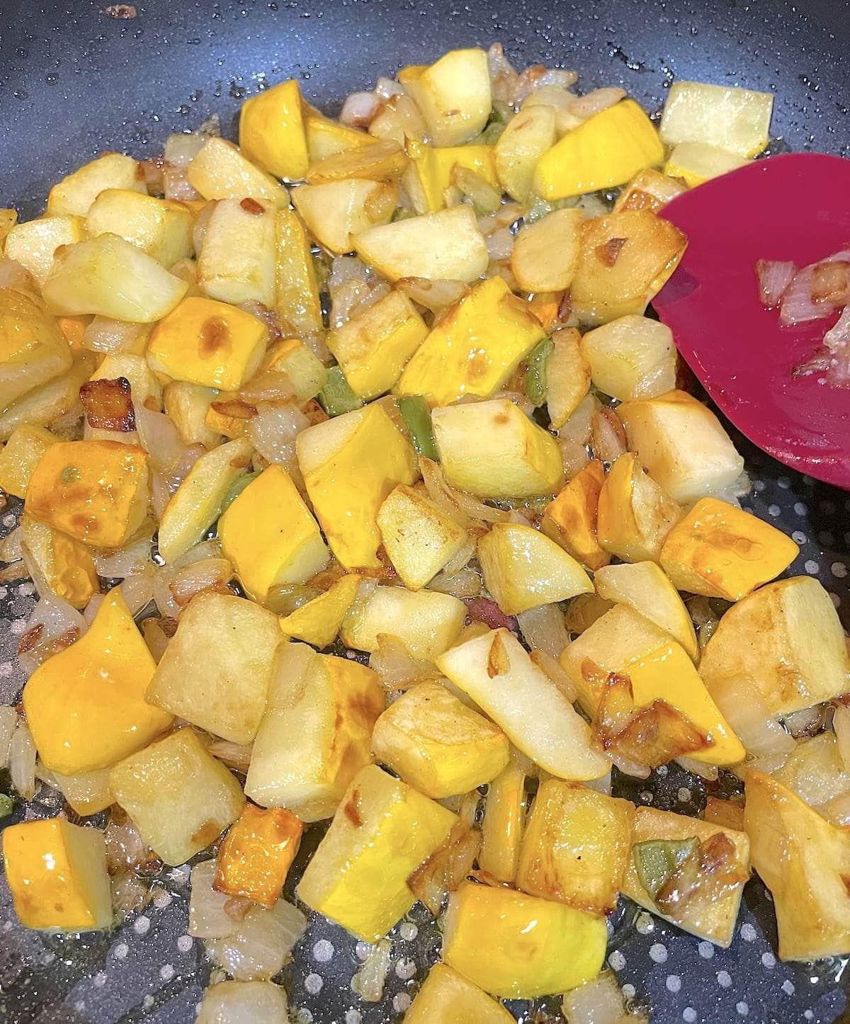 Sauteed patty pan squash in a skillet with peppers, onions, and garlic.