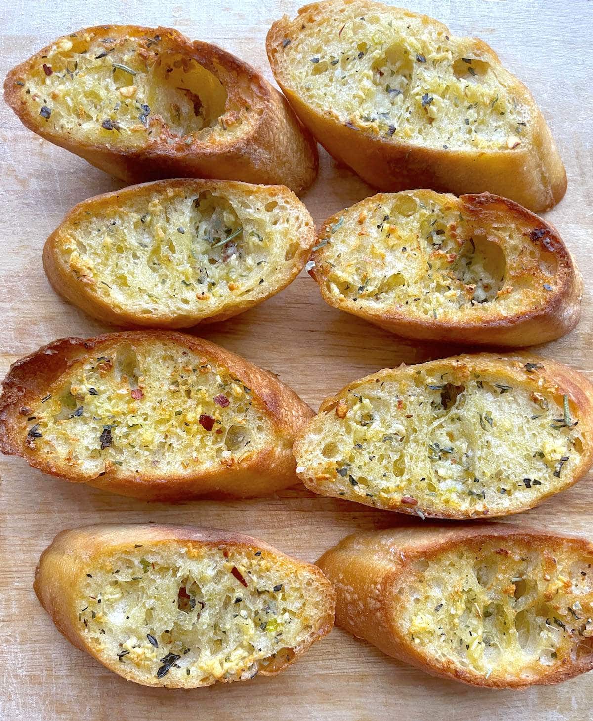 Slices of garlic toast with Italian seasoning on a wood cutting board.