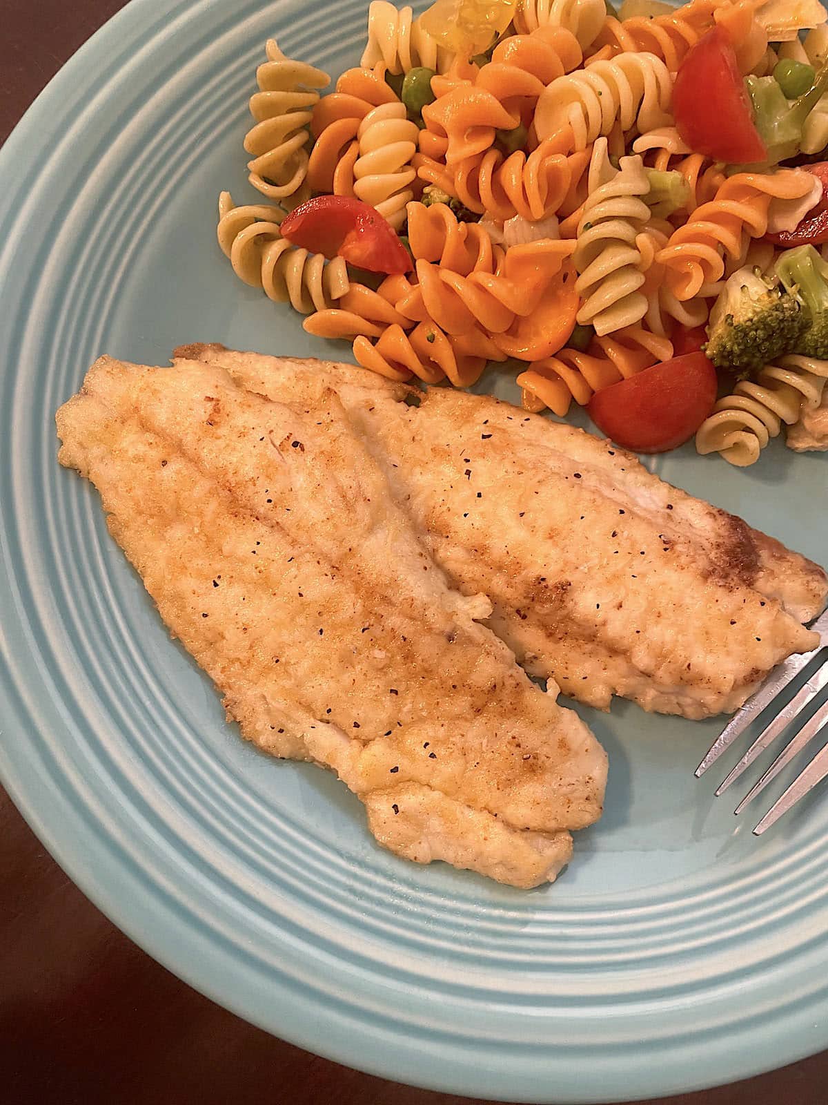 A blue plate with pan fried fish fillets and tri-color pasta salad on it.