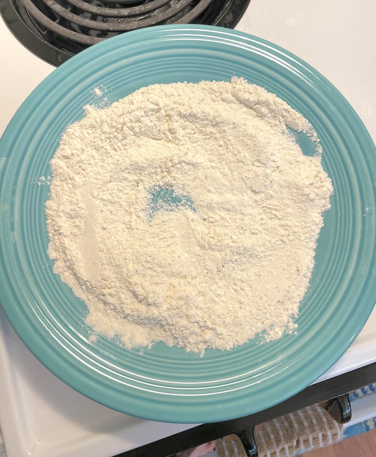 A blue plate with a flour mixture for breading fish fillets on it.