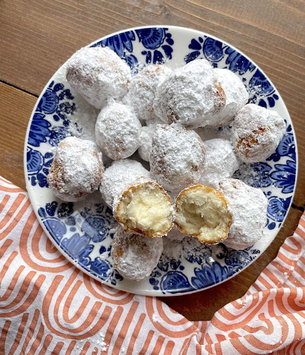 A blue plate with easy biscuit beignets on it, covered in powdered sugar, with one split open on the top.