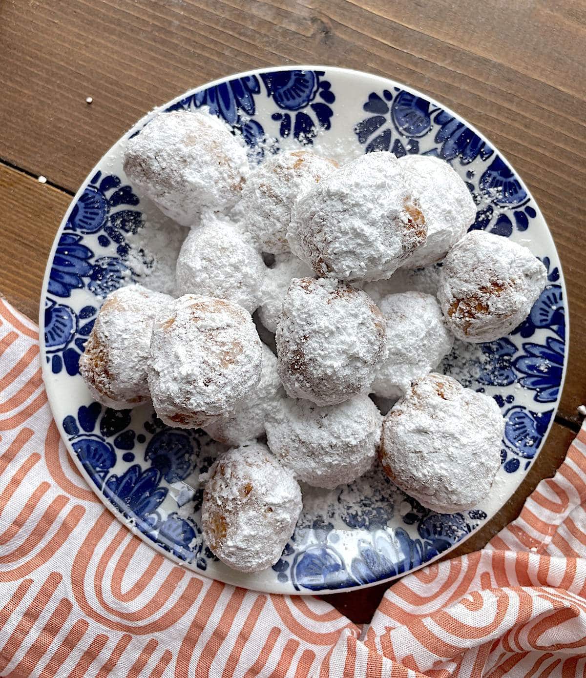 A blue plate with a huge pile of biscuit beignets on it, covered in a huge dusting of powdered sugar.