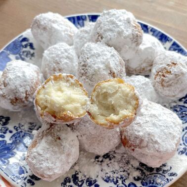 A blue plate with biscuit beignets on it, covered in powdered sugar, with one split open on the top.