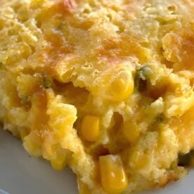 A Facebook image of a slice of jiffy corn pudding on a white place with corn kernels, cheddar cheese, and peppers.