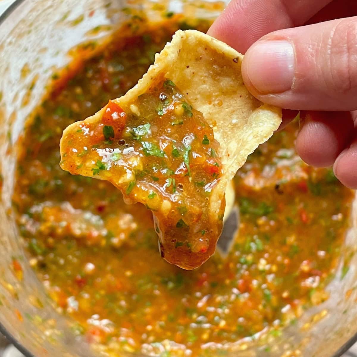 A hand scooping some fire-roasted cherry tomato salsa up with a chip.