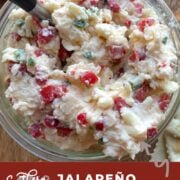 A pin image of a bowl of spicy jalapeño pimento cheese made with white cheddar cheese with a spoon.