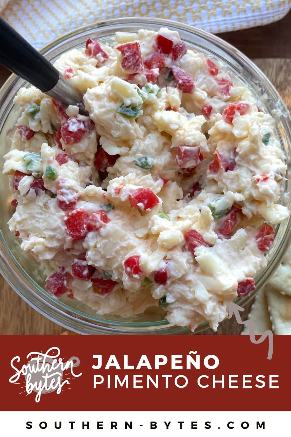 A pin image of a bowl of spicy jalapeño pimento cheese made with white cheddar cheese with a spoon.