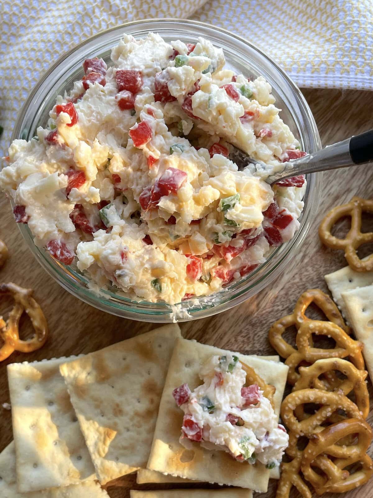 A jar of spicy pimento cheese surrounded by saltines and pretzels.