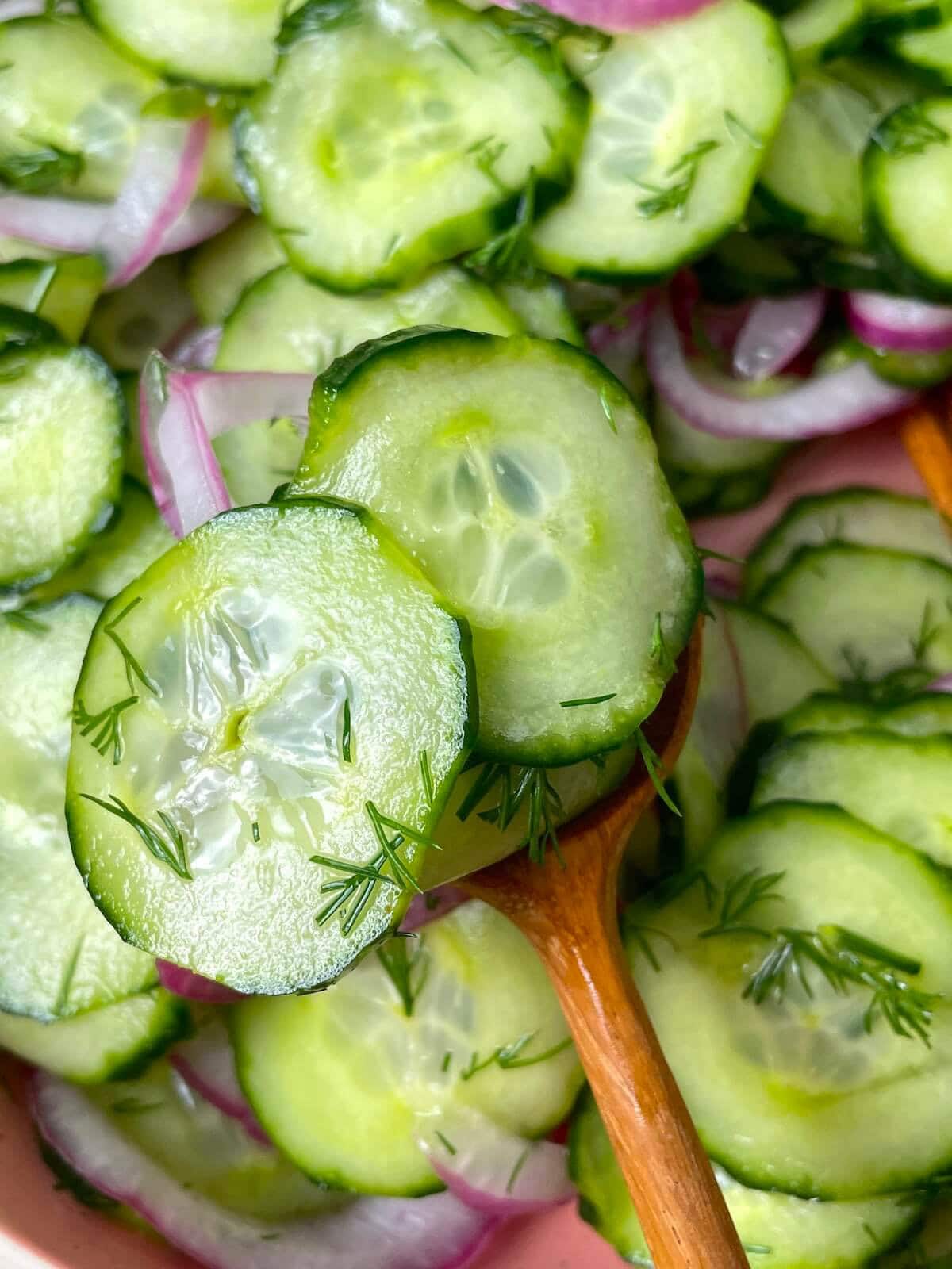 Pickled cucumber salad with red onions being served on a wooden spoon.