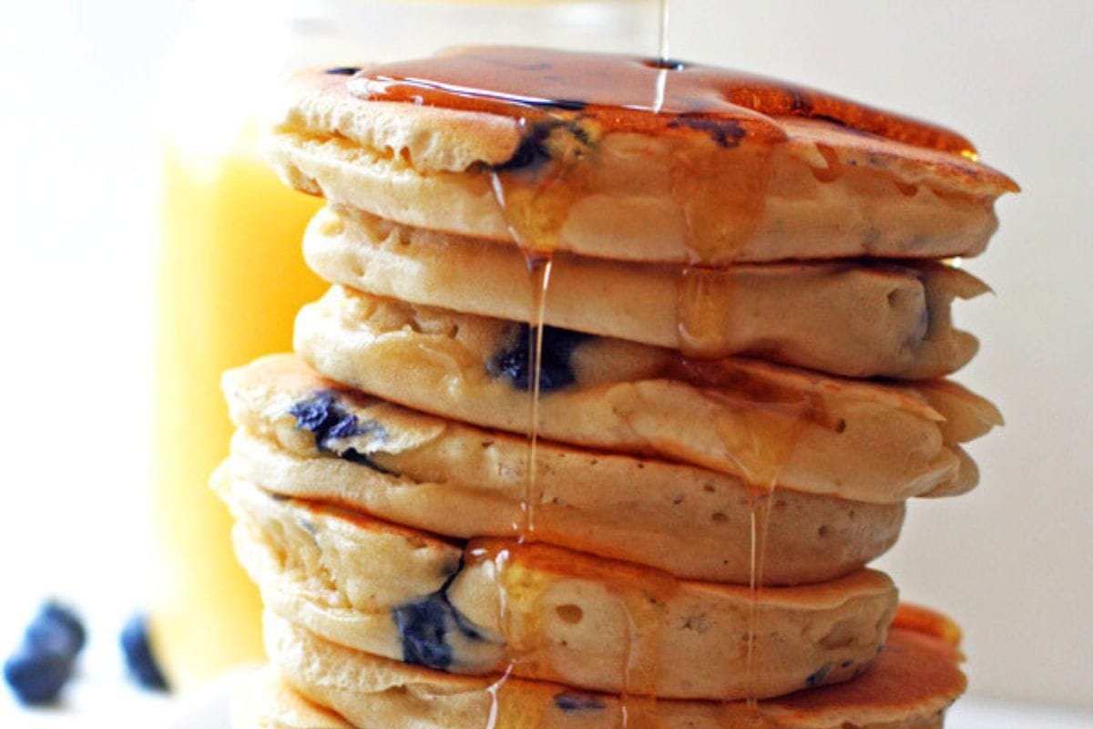 A stack of blueberry pancakes with syrup dripping down the side.