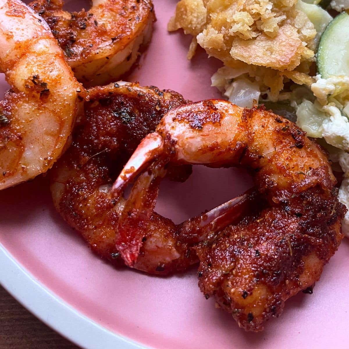 Blackened shrimp with tails on sitting on a pink plate with squash casserole.