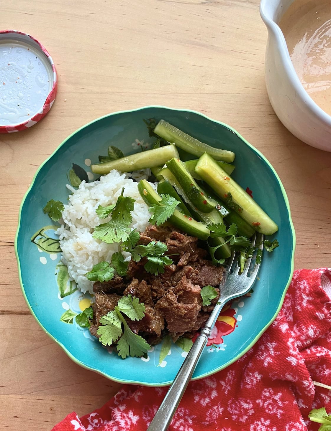 A blue bowl with rice, bulgogi, Korean pickles, and cilantro with Yum Yum sauce on the side.