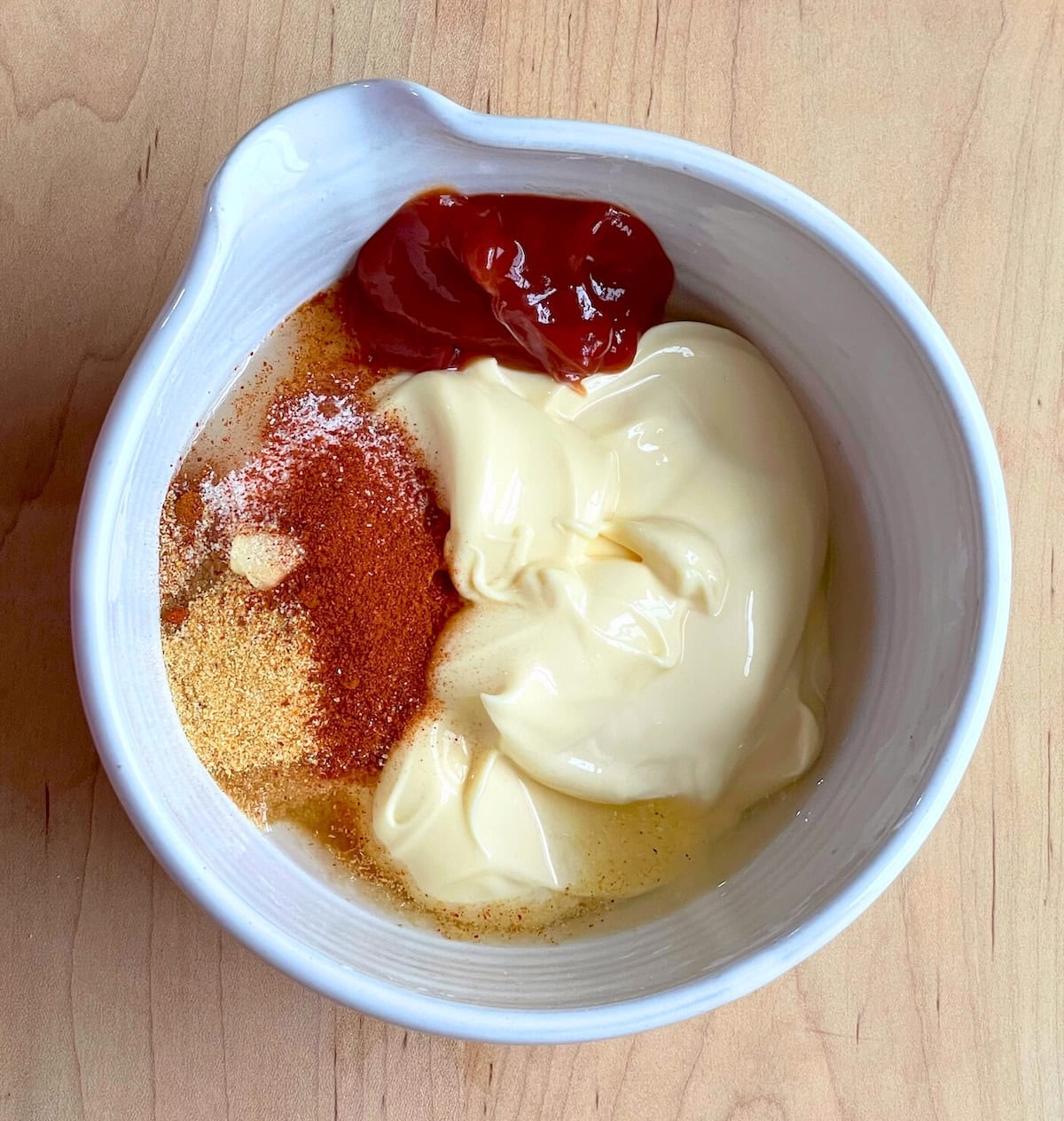 A bowl of the ingredients in yum yum sauce unmixed - ketchup, mayo, garlic powder, smoked paprika, rice vinegar, cayenne pepper, and sugar.