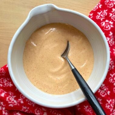 Yum yum sauce in a white bowl with a spoon and a red and white towel.