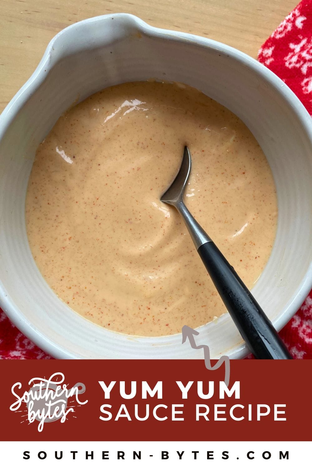 A pin image of a bowl of Yum yum sauce in a white bowl with a spoon and a red and white towel.