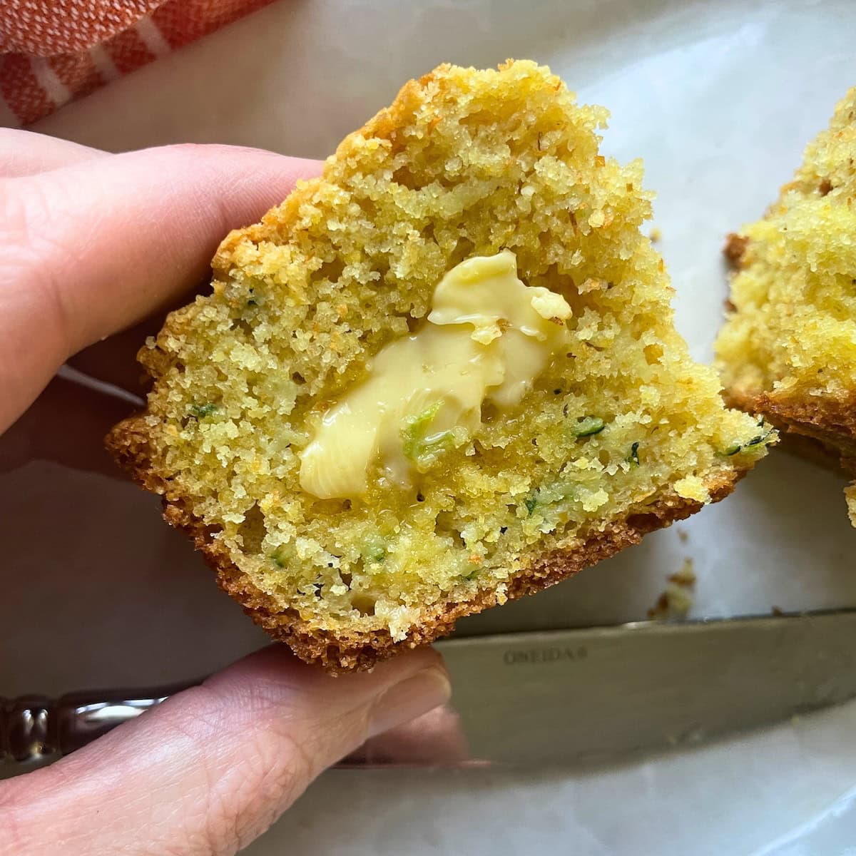 A hand holding a slice of zucchini cornbread that has butter spread on it.