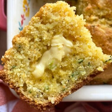 A slice of zucchini cornbread above the pan of cornbread with honey butter melting on it.