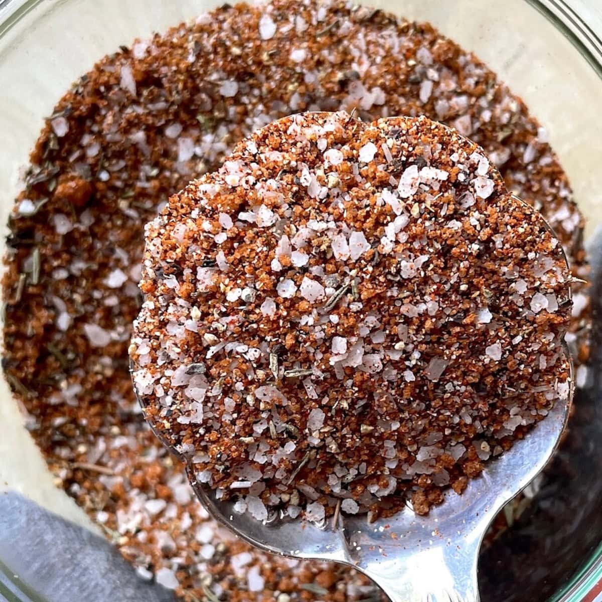 A teaspoon filled with a sweet bbq dry rub seasoning, with a jar of the same seasoning visible in the background.