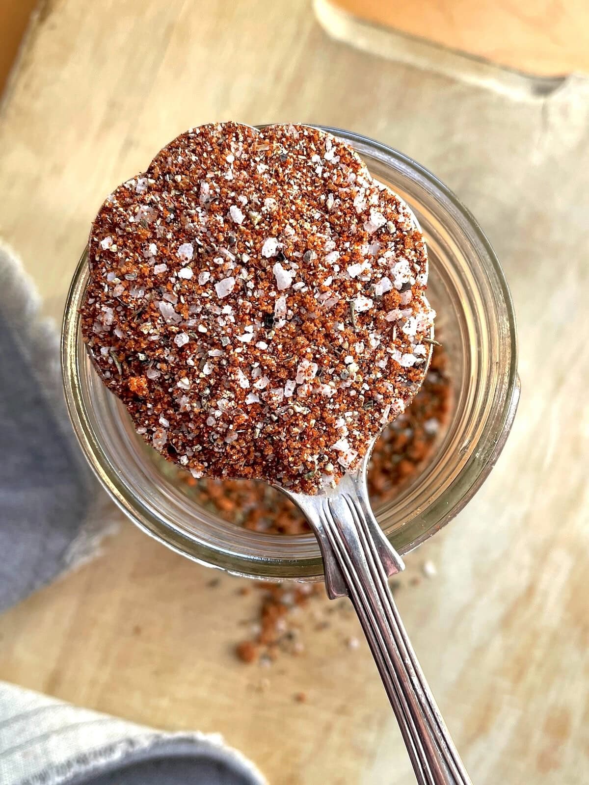 A spoonful of mixed bbq dry rub seasoning with visible salt crystals and spices, taken from above a glass jar.