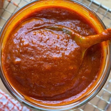 Close-up of a thick, rich homemade barbecue sauce in a glass jar with a spoon.